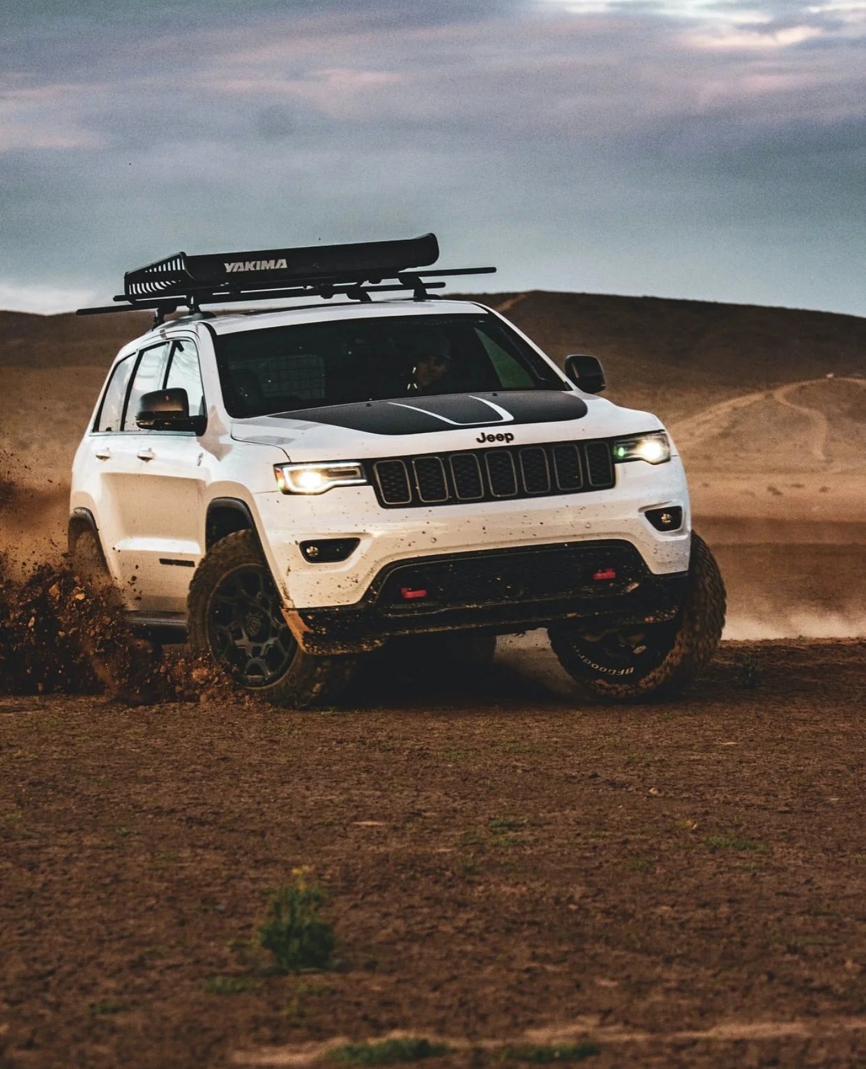A white Jeep Grand Cherokee kicking up dust on a dirt trail