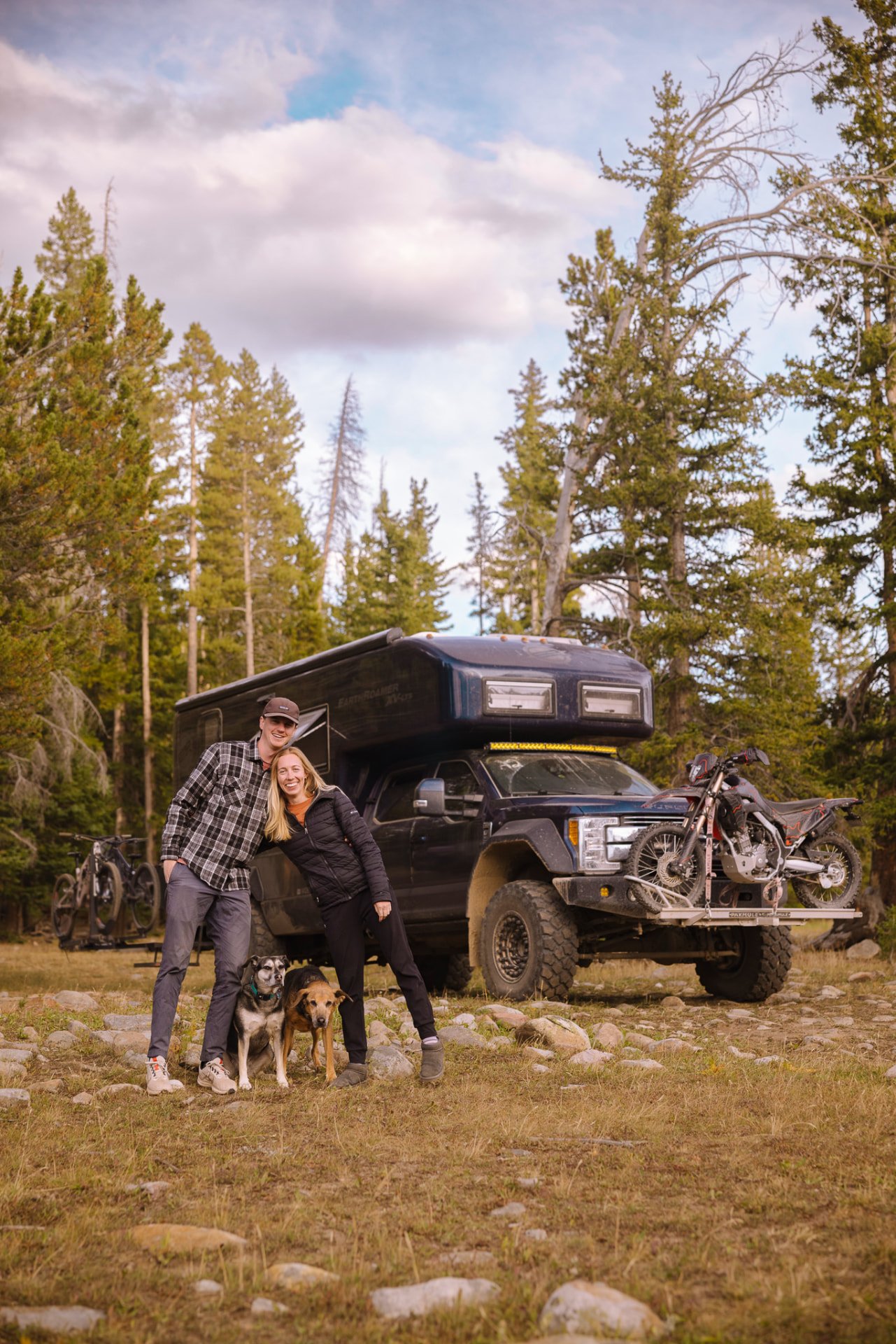 Jacob and Elissa with their two dogs in front of their EarthRoamer overland truck camper in the forest