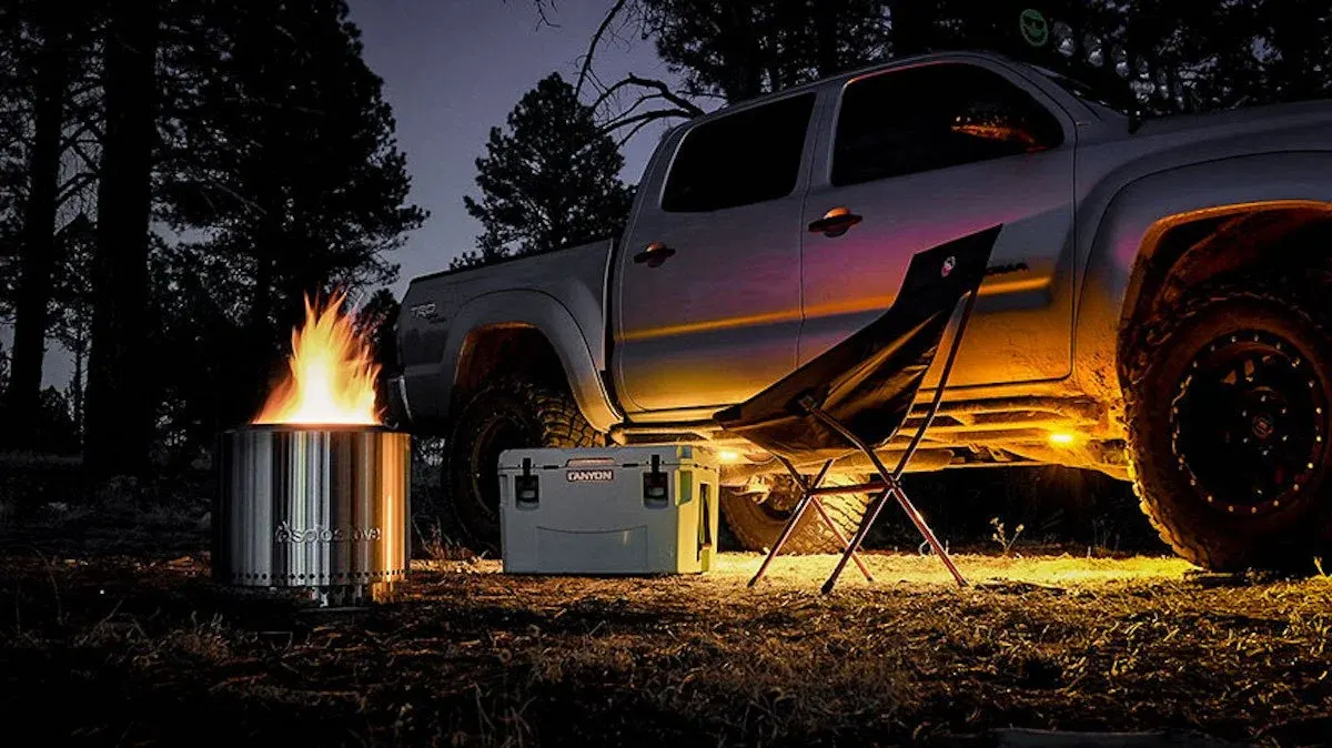 Pickup truck at a night campsite with a fire pit and lights