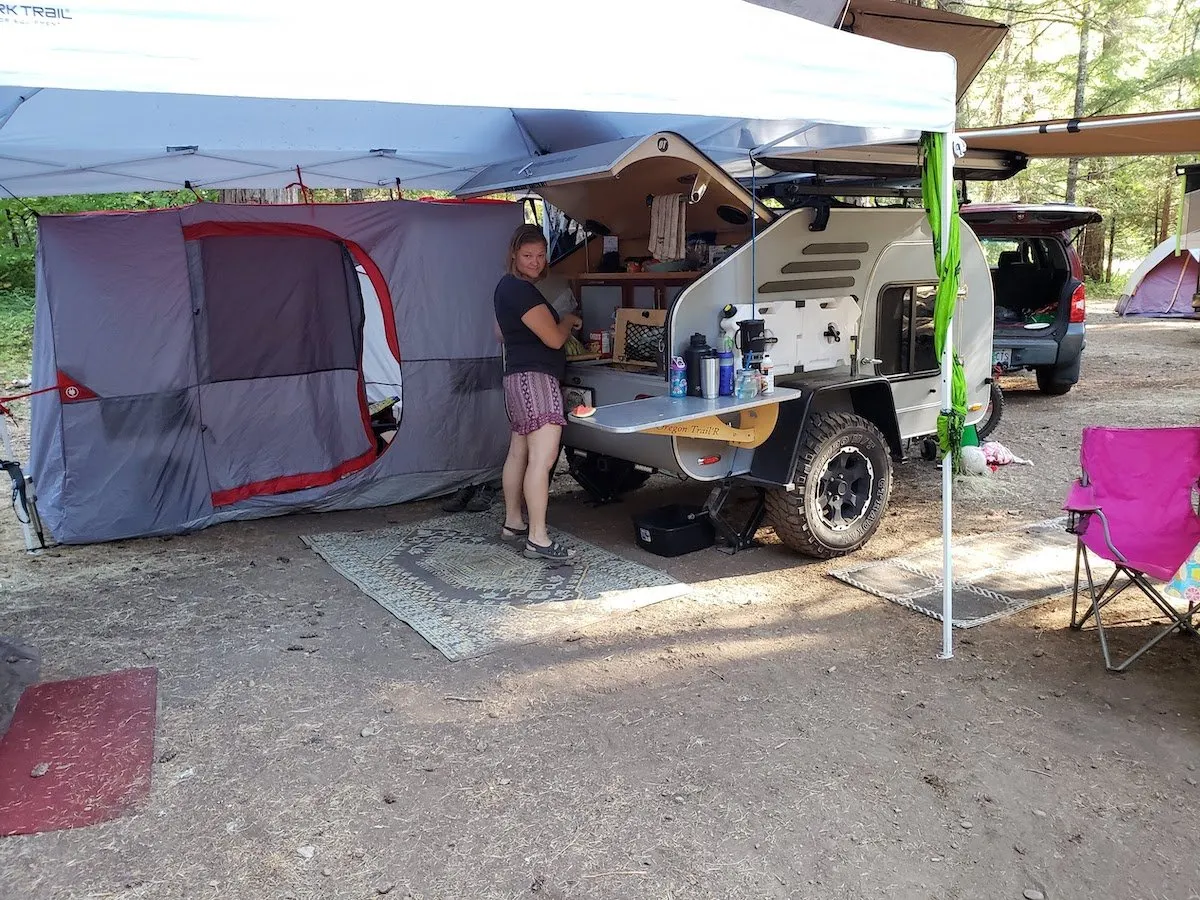 Teardrop camper set up at a campsite with a canopy