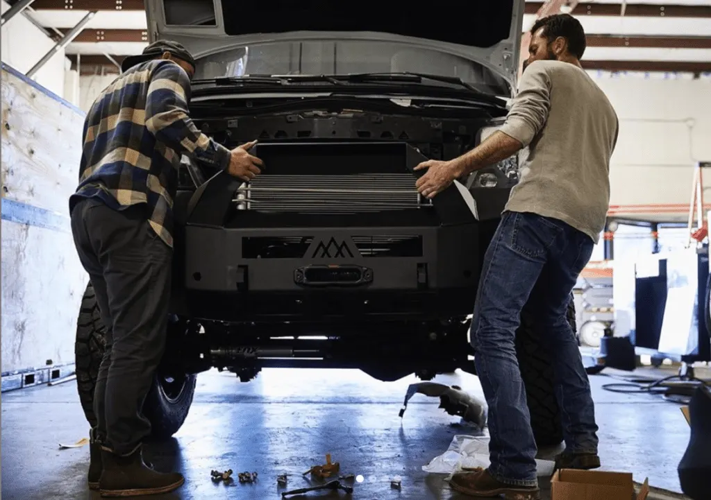 Two men working on the front of a truck in a shop