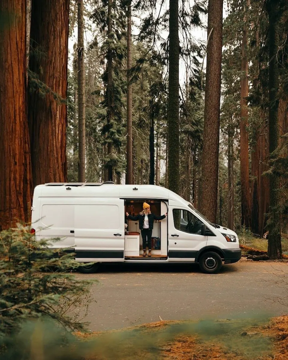 Woman standing in the doorway of a camper van among redwoods