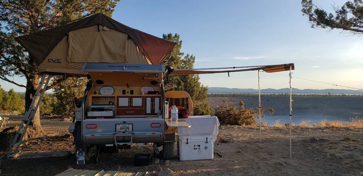 Teardrop trailer with a rooftop tent beside a lake