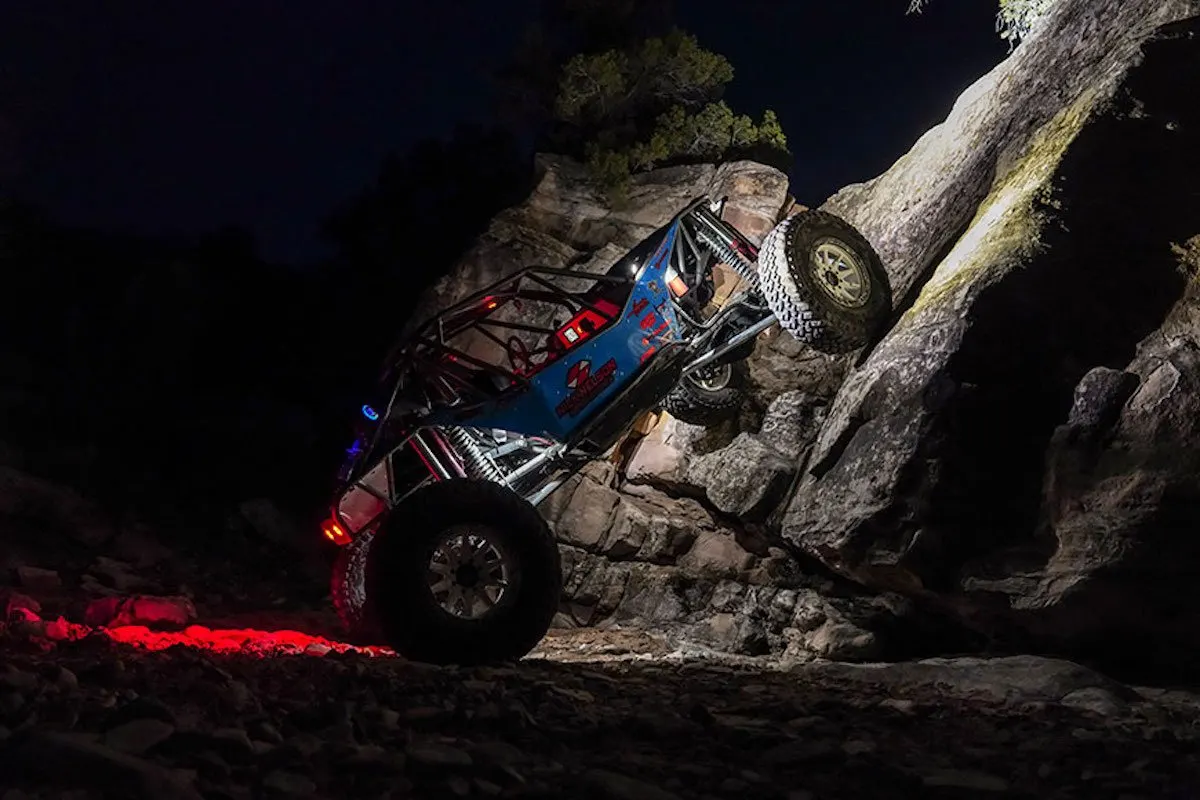 Rock crawler climbing a boulder at night under lights