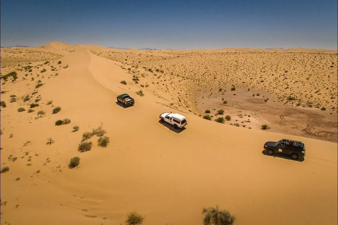 Three overland trucks driving the ridge of a sand dune in Mexico