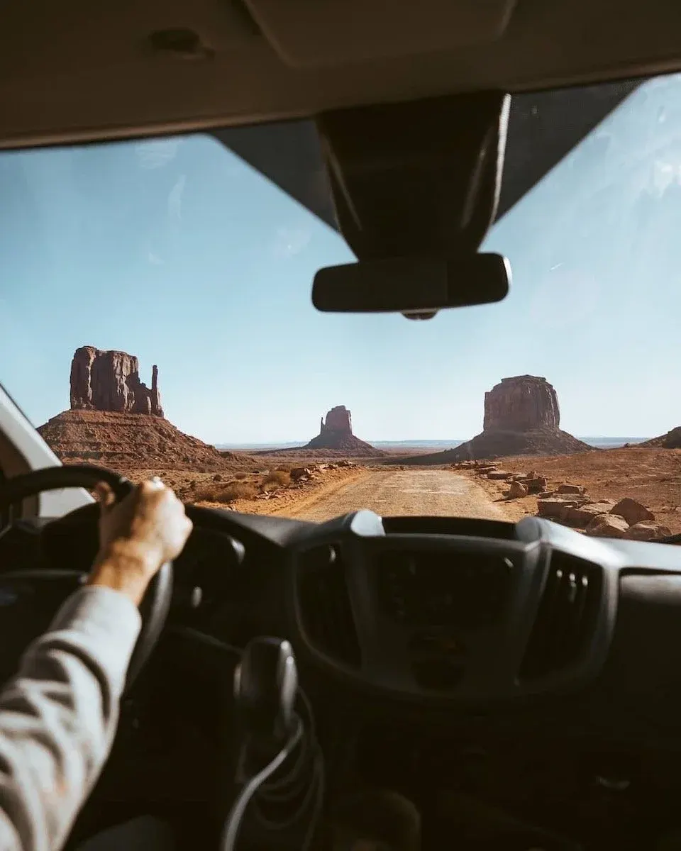 Driver's view through a van windshield toward Monument Valley