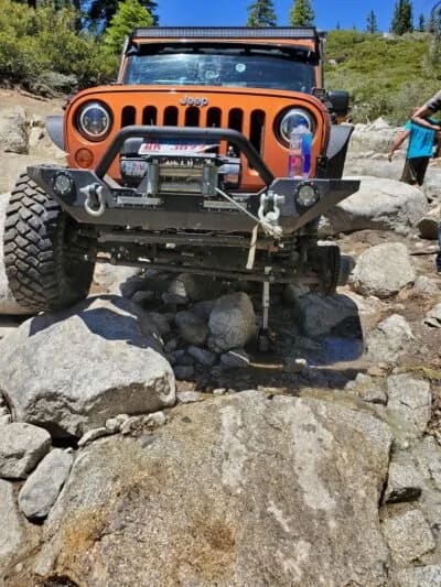 Orange Jeep Wrangler climbing over rocks
