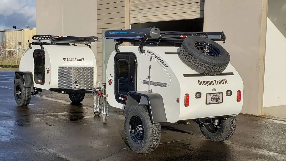 Two white Oregon Trail'R teardrop trailers in a parking lot