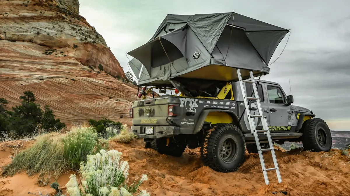 Jeep Gladiator with a rooftop tent and ladder on a desert trail