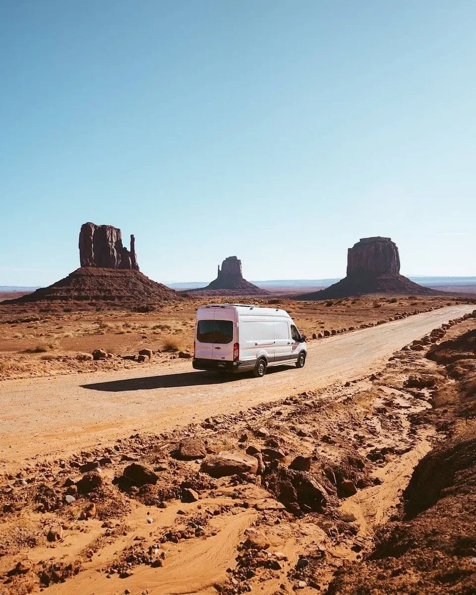 White camper van driving through Monument Valley