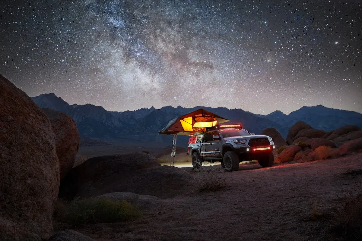 Toyota Tacoma with a lit rooftop tent under the Milky Way