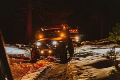 Jeep Wrangler in the snow at night with lights on