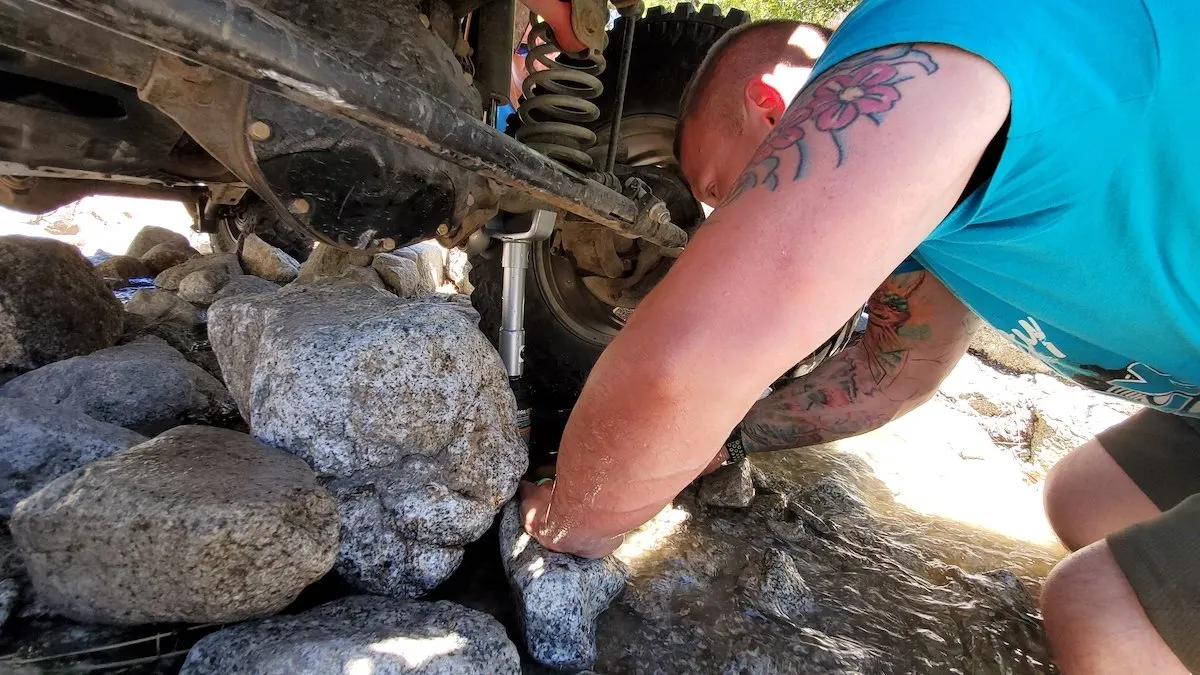 Man placing a jack under a vehicle on a rocky trail