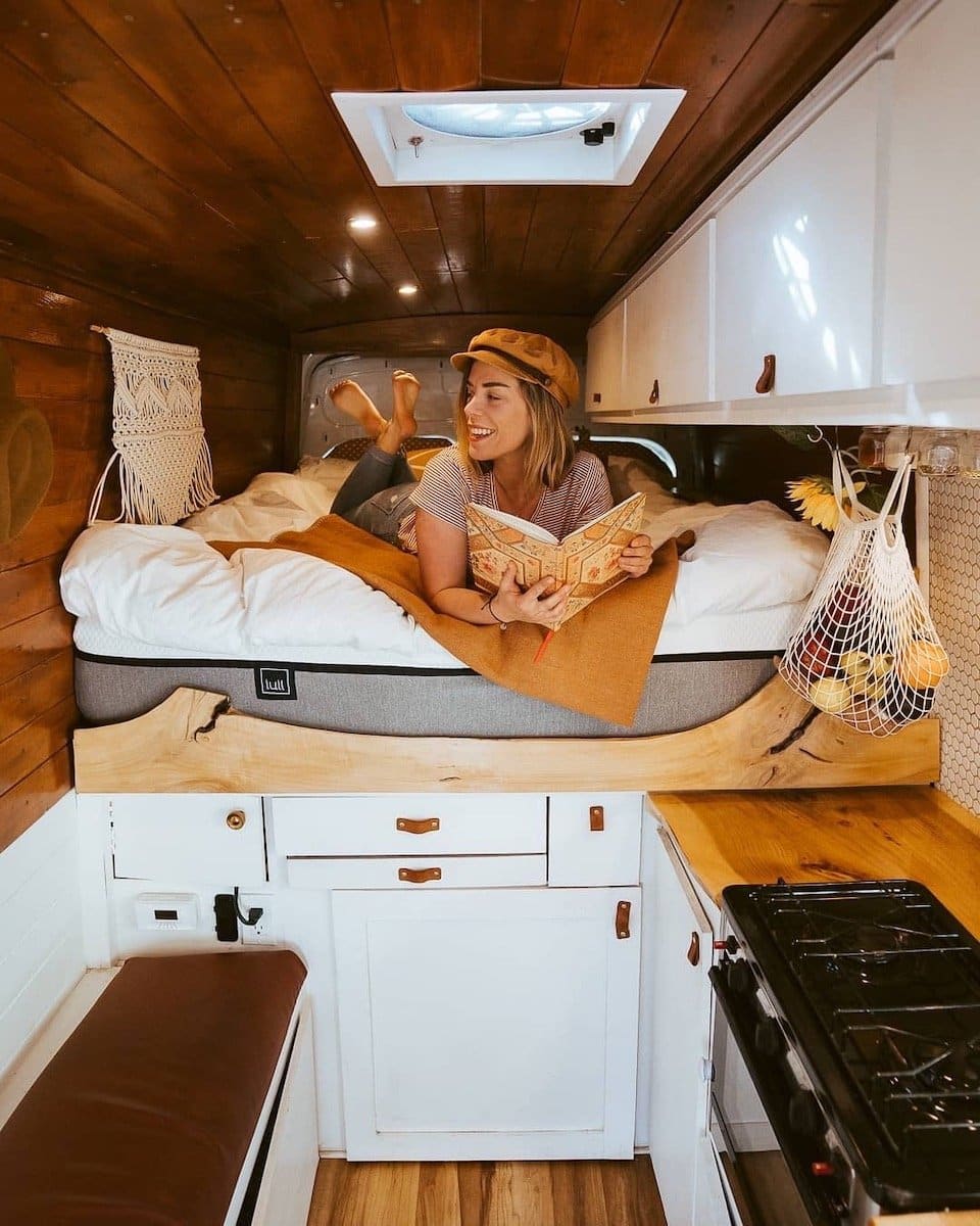 Woman relaxing on the bed inside a converted camper van